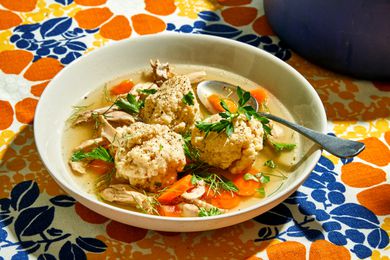 Matzo ball soup in a white bowl with a spoon on a flowered tablecloth