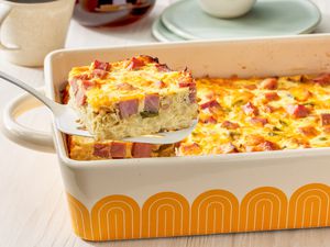 Slice of Denver omelette hashbrown casserole lifted from a casserole dish, and in the surroundings, a stack of plates and a mug