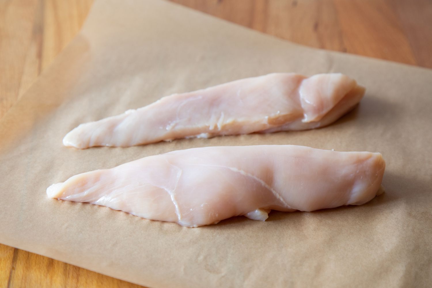 Two chicken tenders on a parchment to make a poached chicken recipe.
