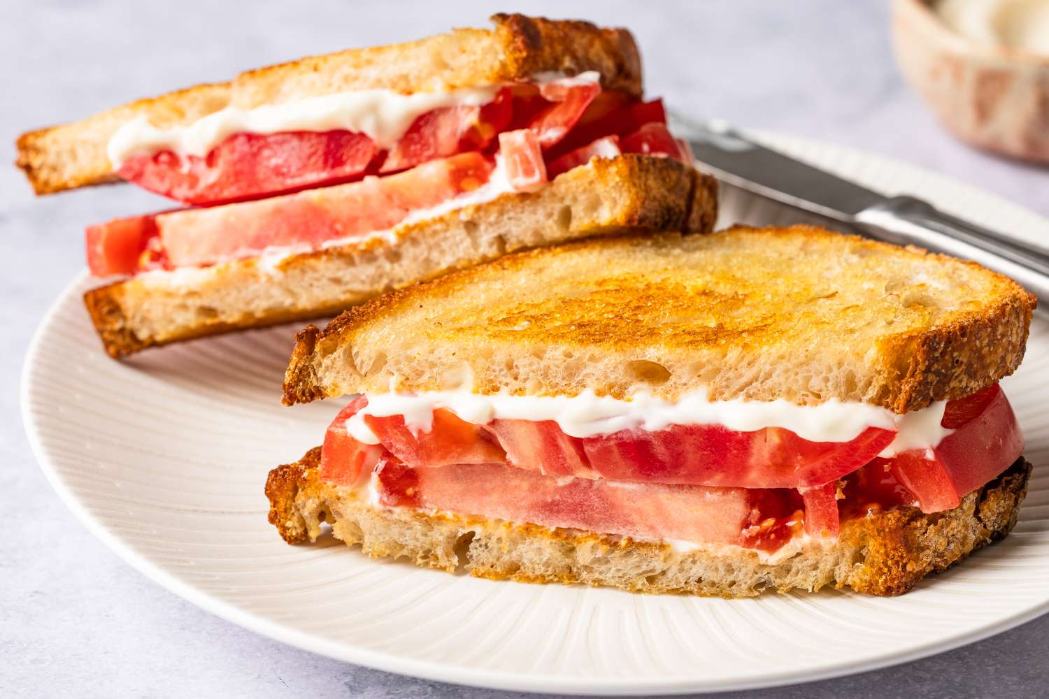 Two tomato sandwiches on a plate, prepared with toasted bread and a creamy spread