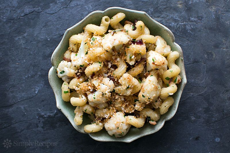 A bowl of pasta with cauliflower and breadcrumbs served in a green dish