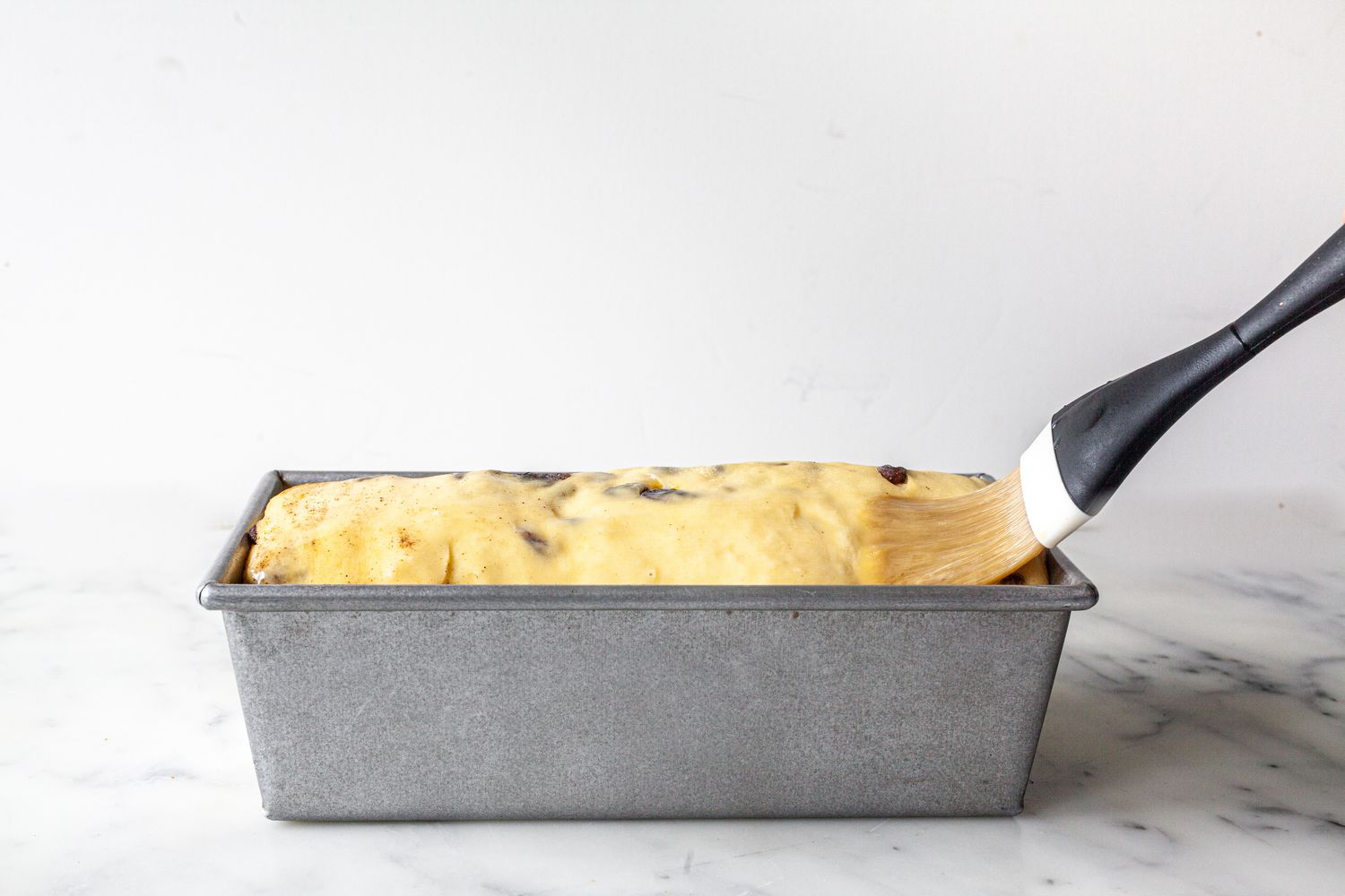 Egg Wash Applied to Cinnamon Swirl Raisin Brioche Loaf Using Pastry Brush in Baking Pan