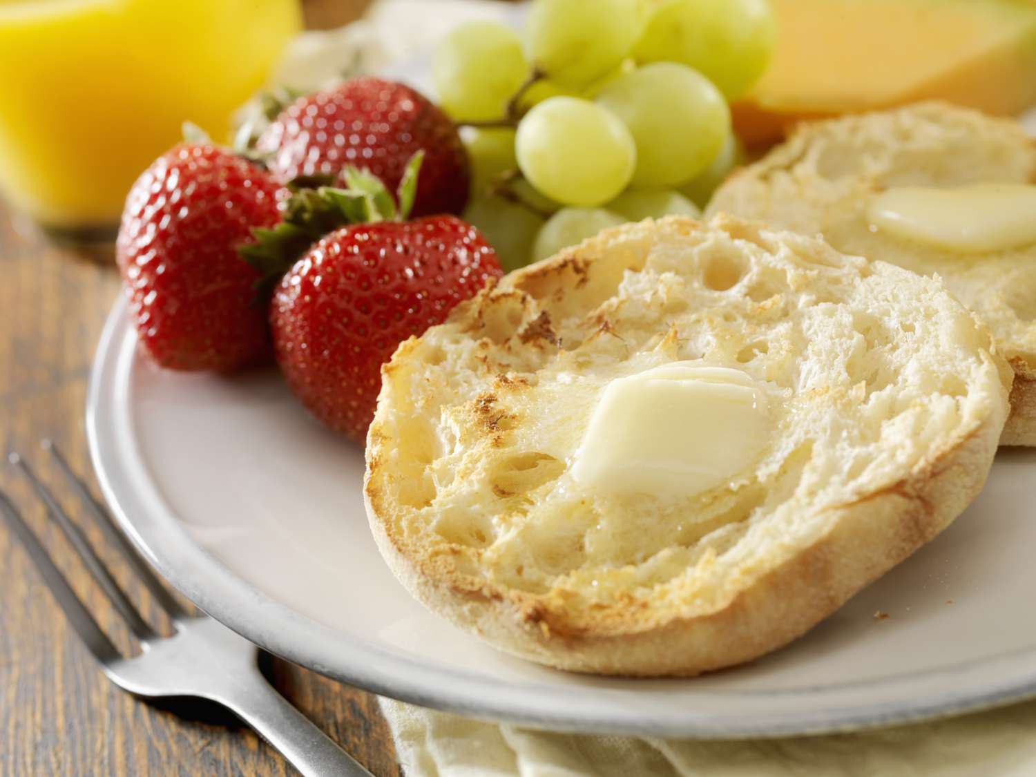 Close-up of an English muffin with melting butter; strawberries and grapes are on the same plate