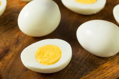 peeled hard boiled eggs on a wood surface, one cut in half