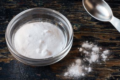 A small glass bowl of baking powder with a measuring spoon on a wood surface