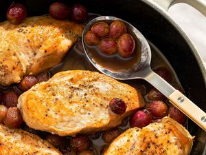 Cooked chicken breasts in a pan with grapes and balsamic sauce a serving spoon holding grapes and sauce