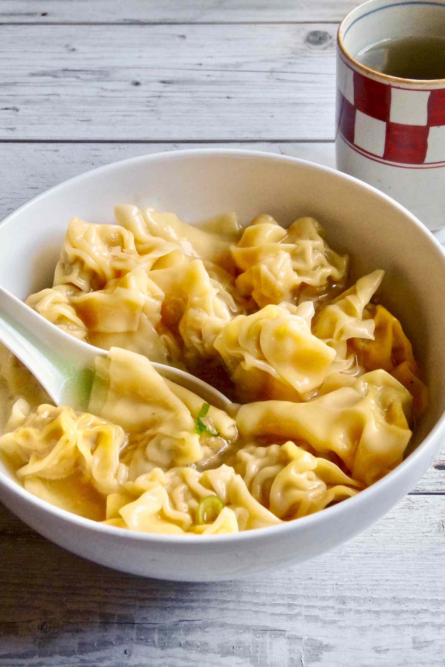 Side view of a bowl of pork and ginger wontons in chicken soup.
