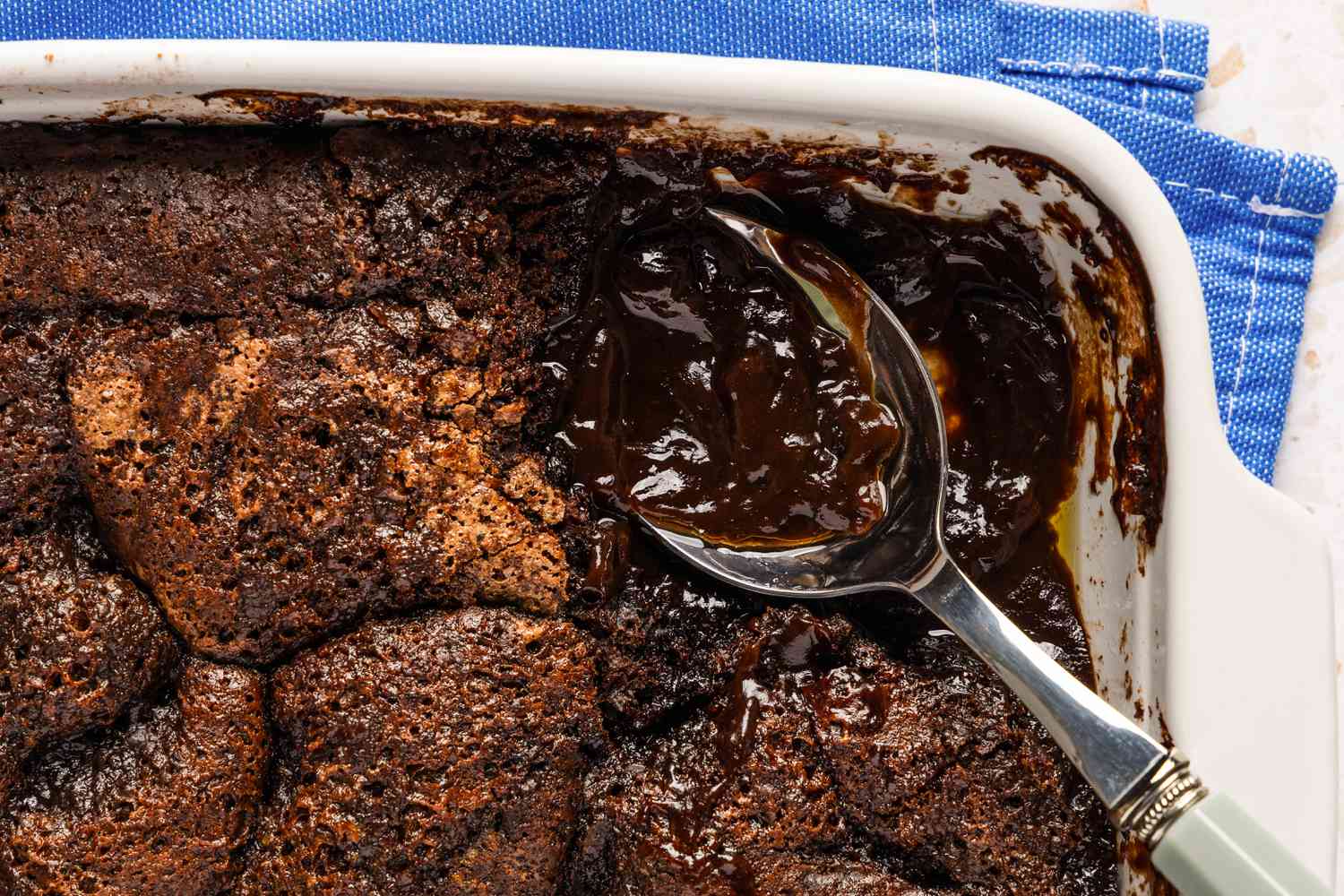 A closeup of chocolate cobbler in a baking dish, with a spoon in one corner where a serving has been scooped out