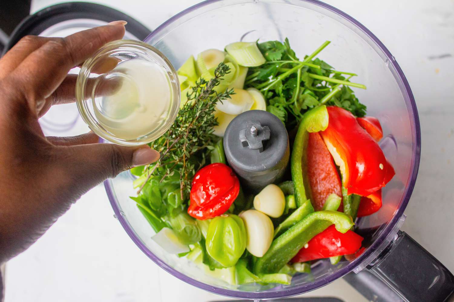 Apple cider vinegar added to onion, bell peppers, celery, and leeks in food processor for Haitian epis recipe