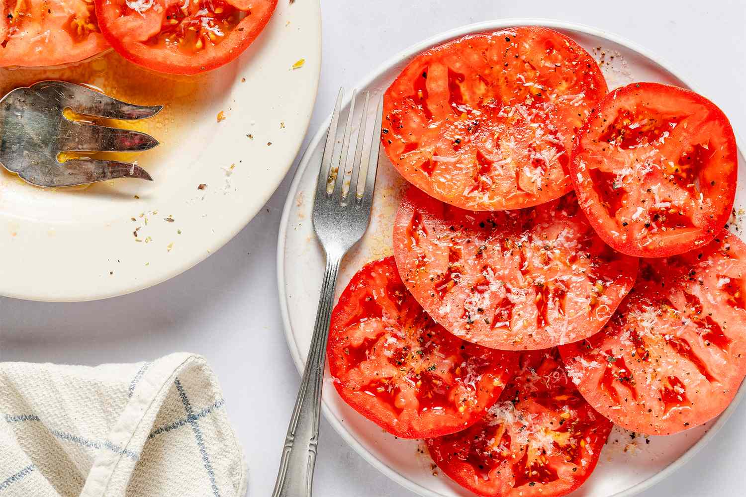 Sliced tomatoes on a plate sprinkled with spices accompanied by a fork and a napkin