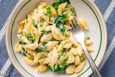 A bowl of creamy pasta with peas and spinach, garnished with cheese and accompanied by a fork