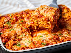 A baked lasagna tray with a portion being lifted out with a spatula layers of pasta cheese and meat visible