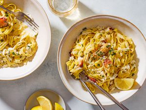 Overhead shot of two bowls with 5-ingredient creamy crab pasta, with a lemon wedge and chopped fresh tarragon as garnish