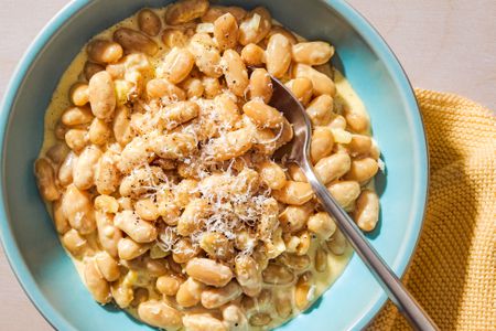 Overhead view of a teal colored bowl of Alfredo Beans with a spoon and topped with shredded Parmesan