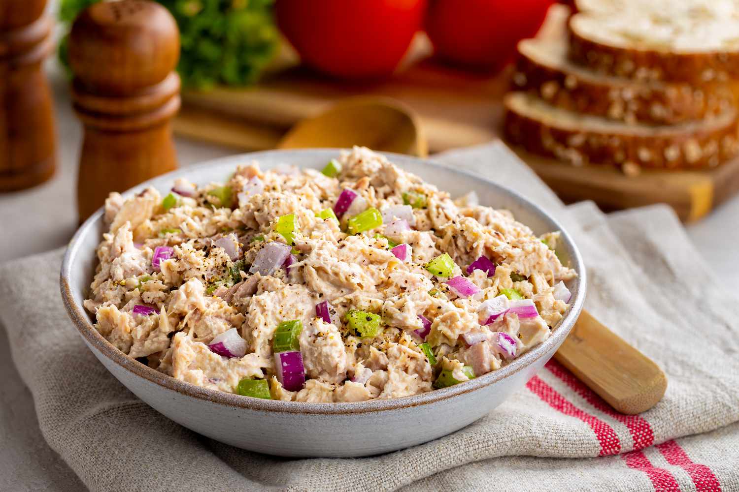 bowl of tuna salad, sitting on a kitchen towel, and in the background, ingredients on a cutting board