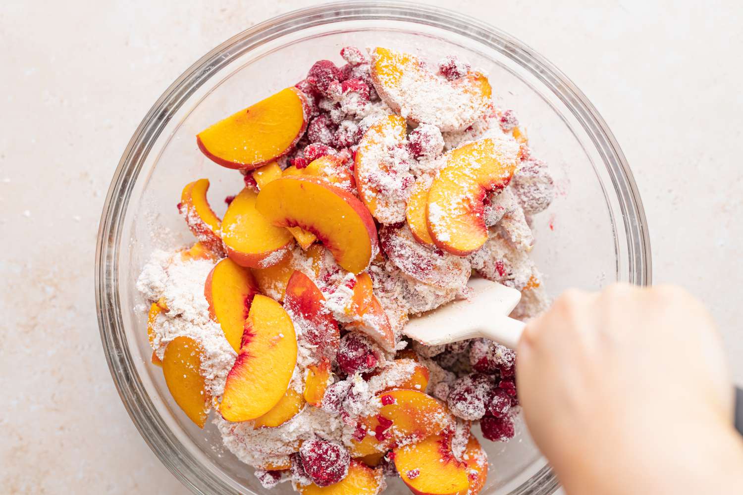 Mixing the filling of sliced peaches and raspberries for a stone fruit and berry pie.
