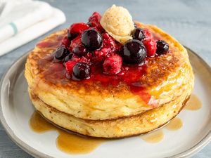 Pancakes topped with mixed berries syrup and a dollop of butter on a plate