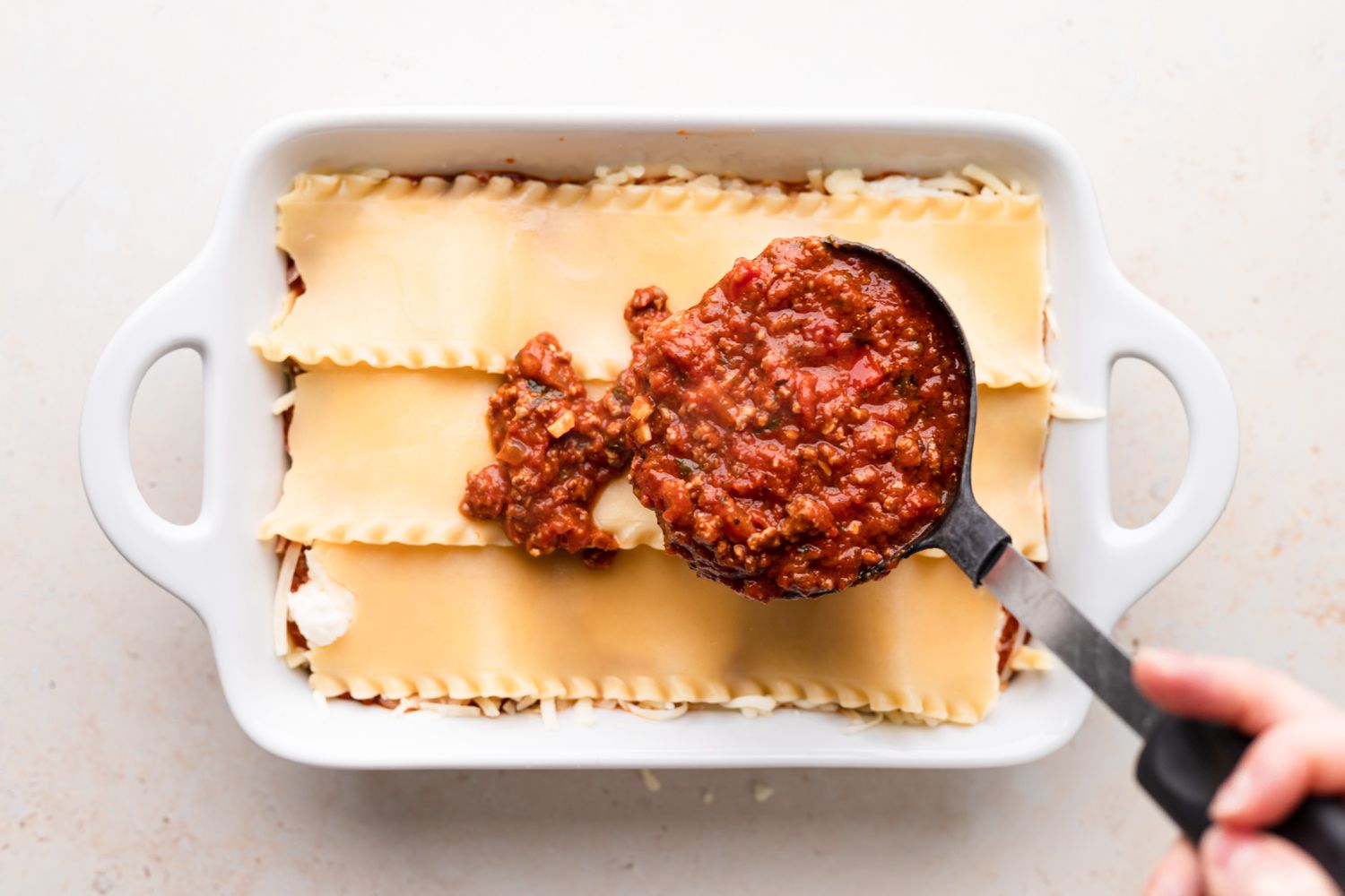 Layering sauce over noodles to make the best lasagna recipe.