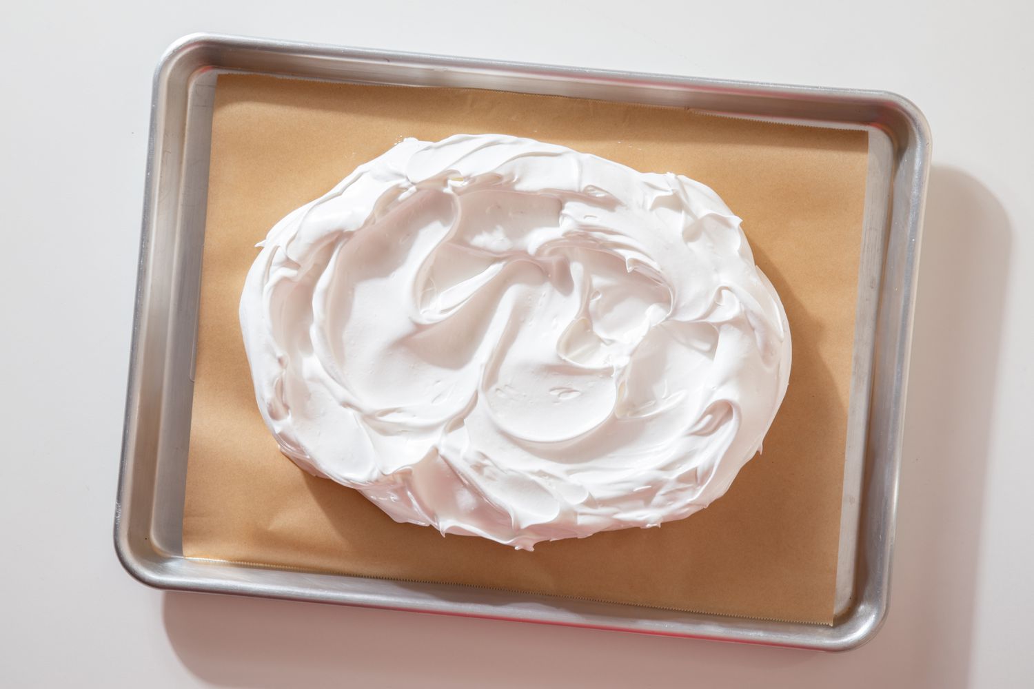 meringue spread into a flatter layer on the parchment paper-lined baking sheet for showstopper berry pavlova recipe