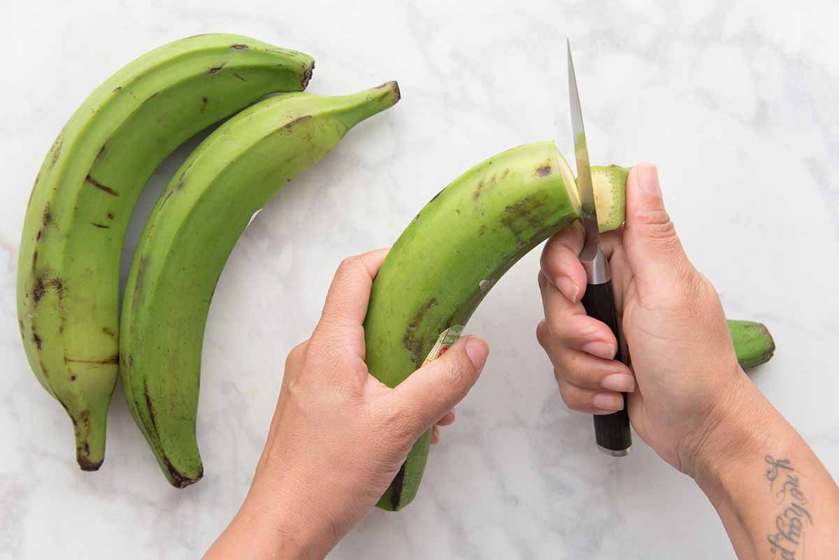 Person cutting the top off of a green plaintain.