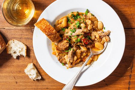 Bowl of cassoulet with bread and white wine.