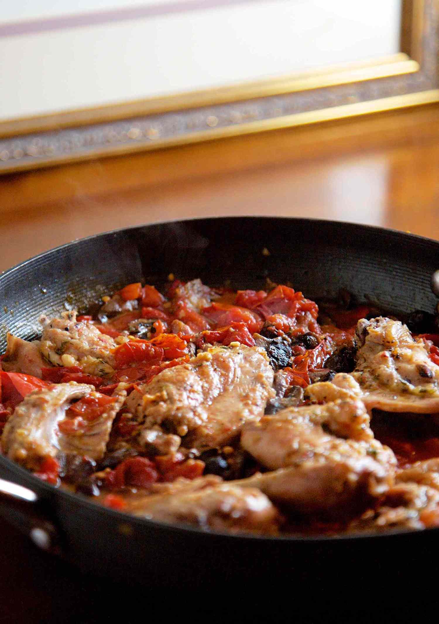 A pan containing rabbit cacciatore with ingredients like tomatoes and olives visible