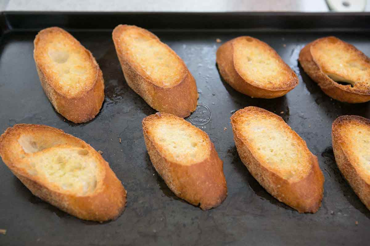 Slices of french bread resting on a baking sheet 