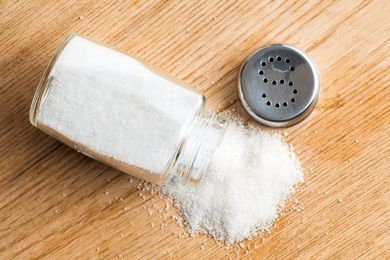 A spilled salt shaker with salt on a wooden surface
