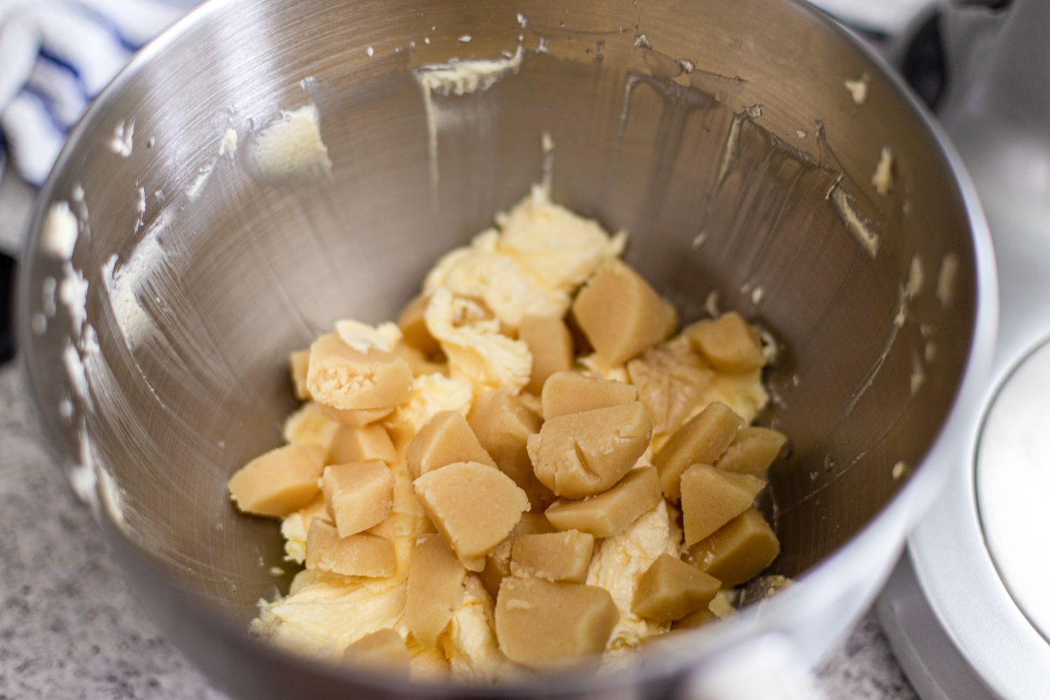 Adding almond paste to butter and sugar in a bowl to make marzipan stamped cookies.