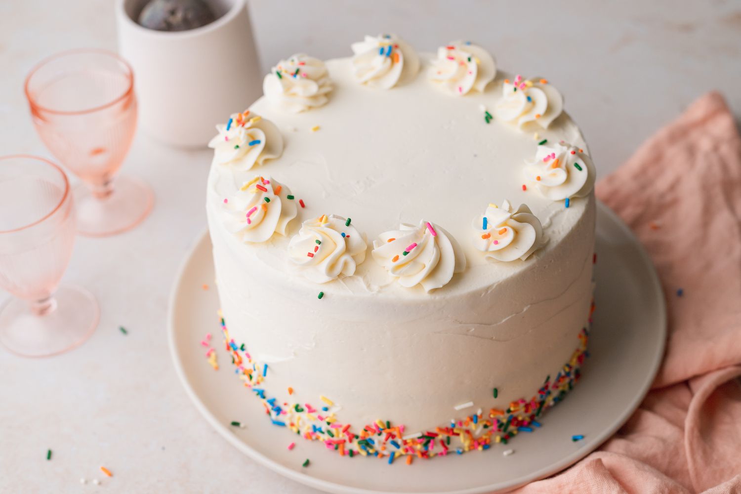 Decorated Rainbow Layer Cake on a Plate with Glasses in Background