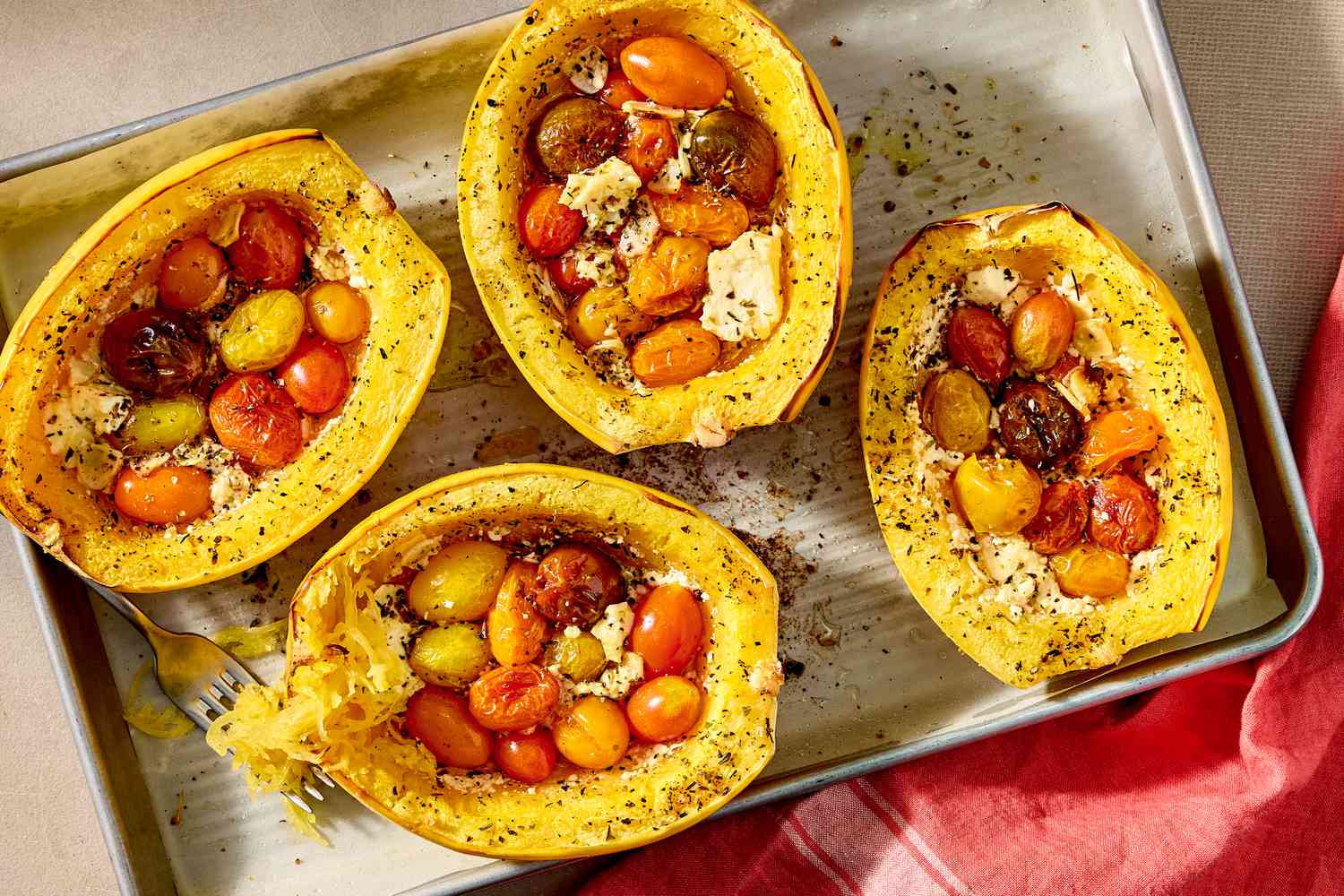 Overhead shot of four baked spaghetti squash stuffed with feta and cherry tomatoes, on a baking sheet