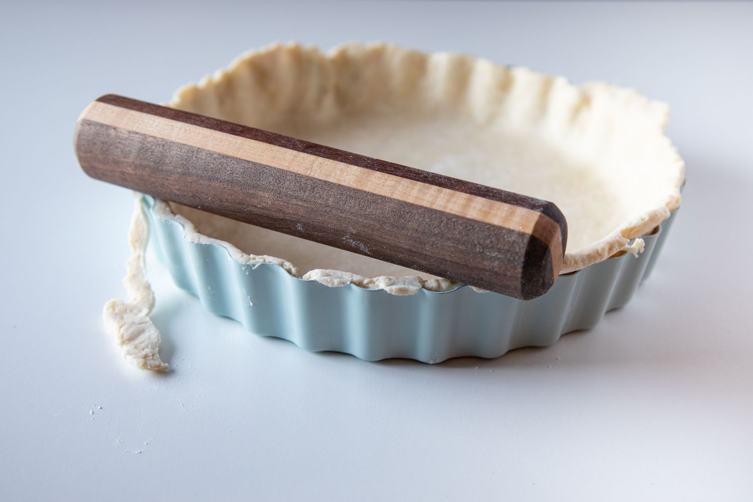 Rolling a rolling pin over the top of a tart crust to make a quiche lorraine recipe.