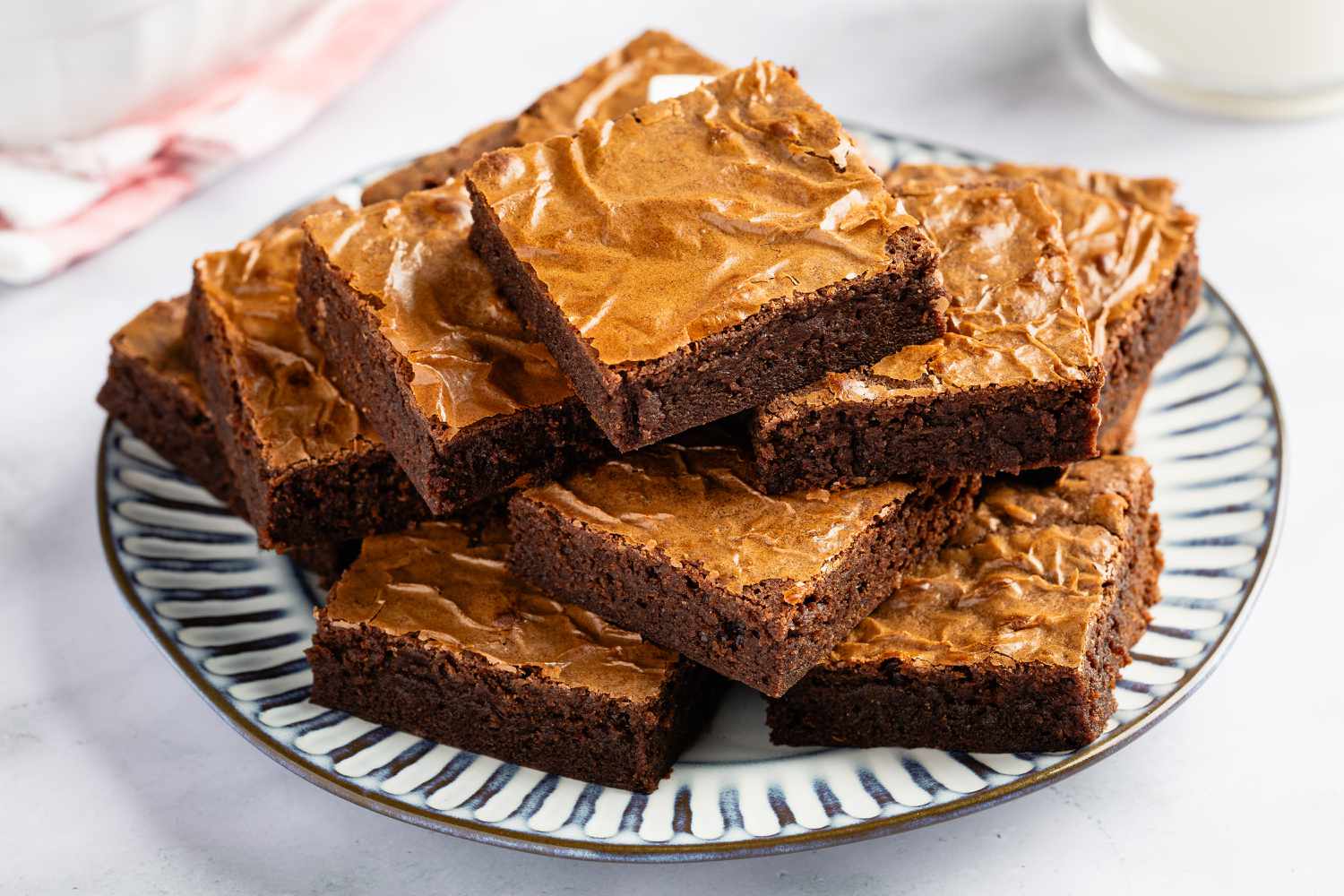 Angle view of a brown and white plate on a marble countertop with a stack of brownies cut into squares