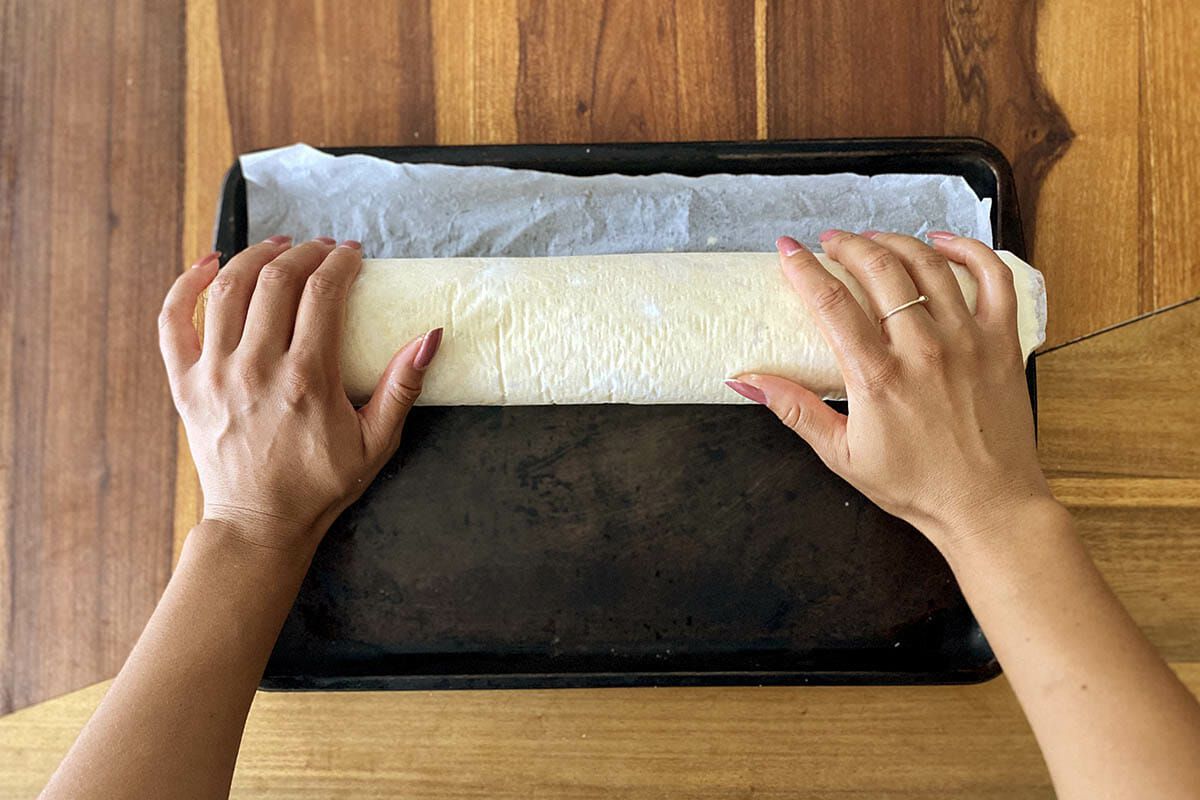 Easy gluten free cinnamon rolls being rolled in parchment paper.