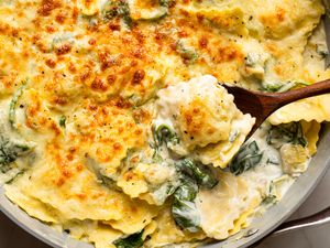 Cheesy spinach and artichoke ravioli cooked in a pan with a wooden spoon