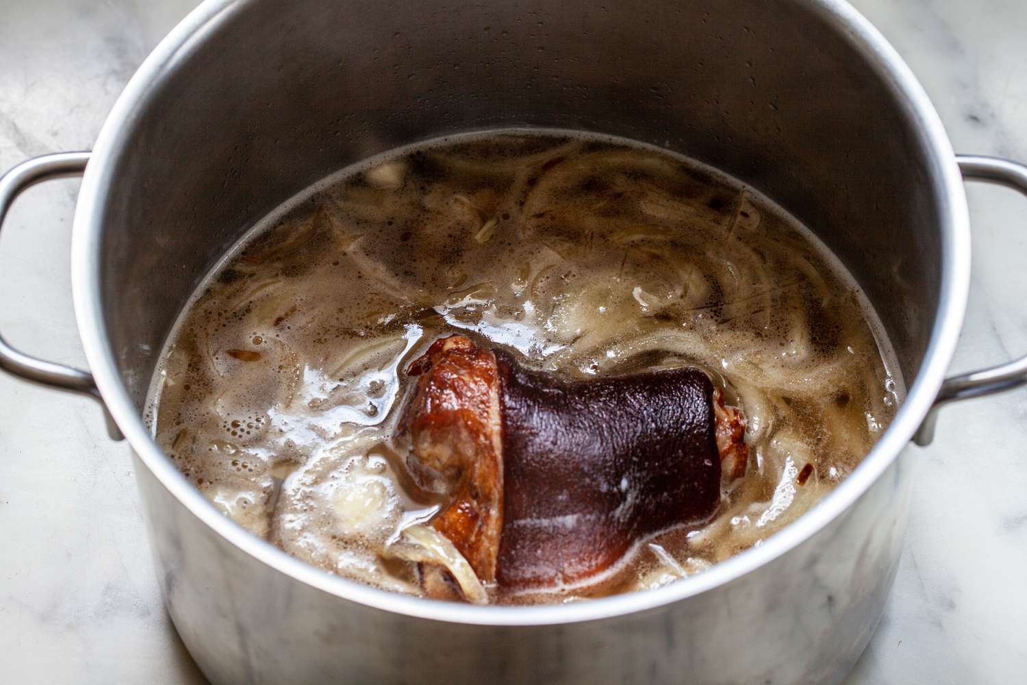 Ham hock and liquid added to a stockpot to show how to make collard greens.