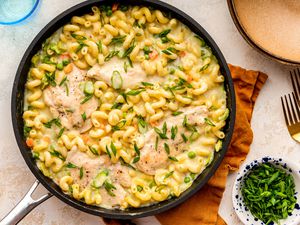 easy chicken primavera at a table setting with a bowl of sliced green onions, a bowl, and utensils on the counter