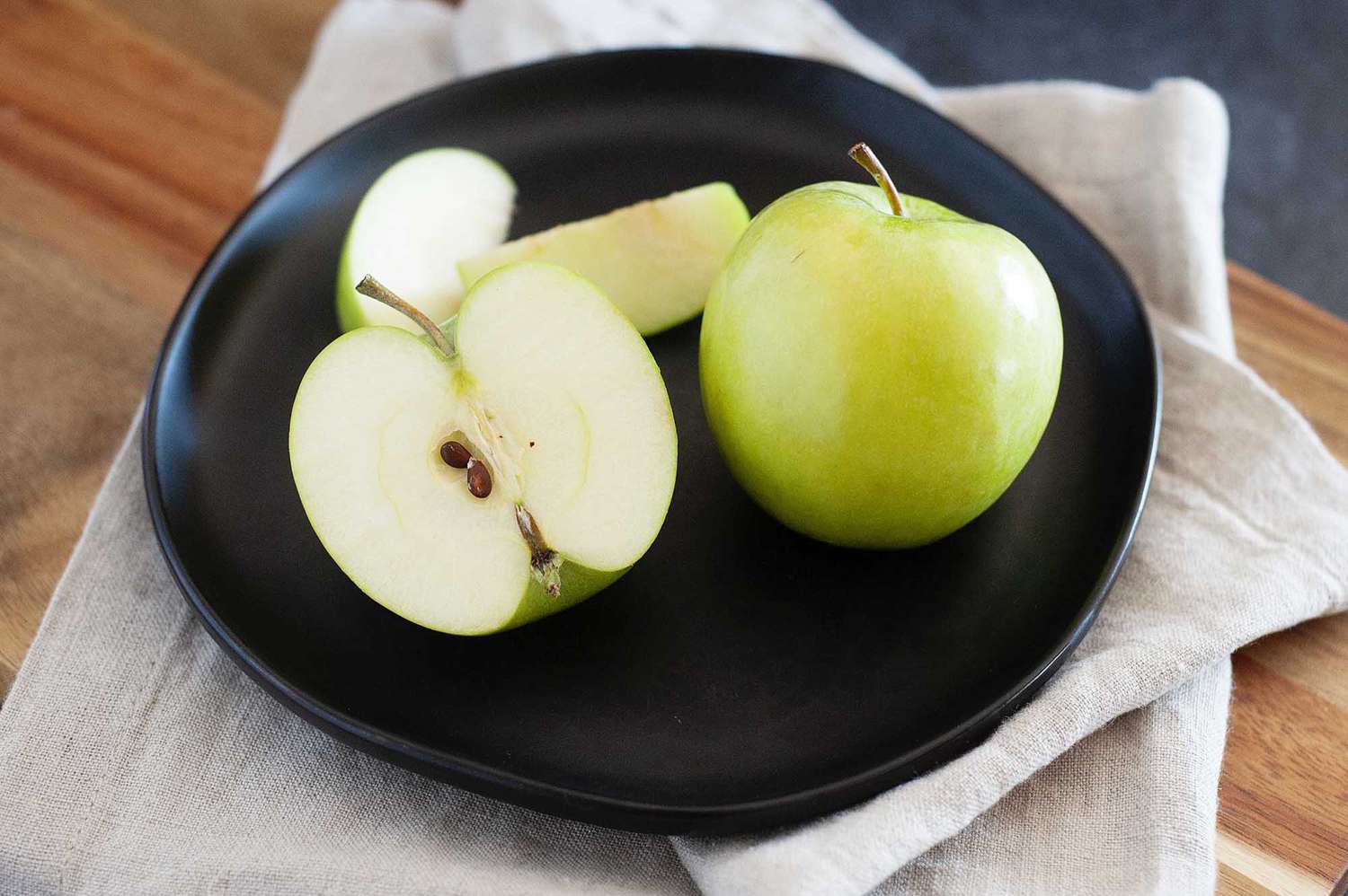 Granny smith apples, one of the best apples for pie, is set on a plate. The apple on the left is sliced in half.