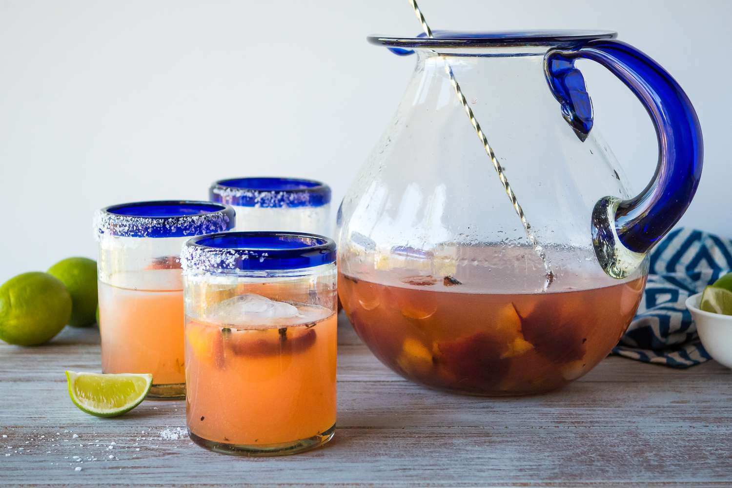 Three grilled peach pitcher margaritas on a table with limes and a pitcher.
