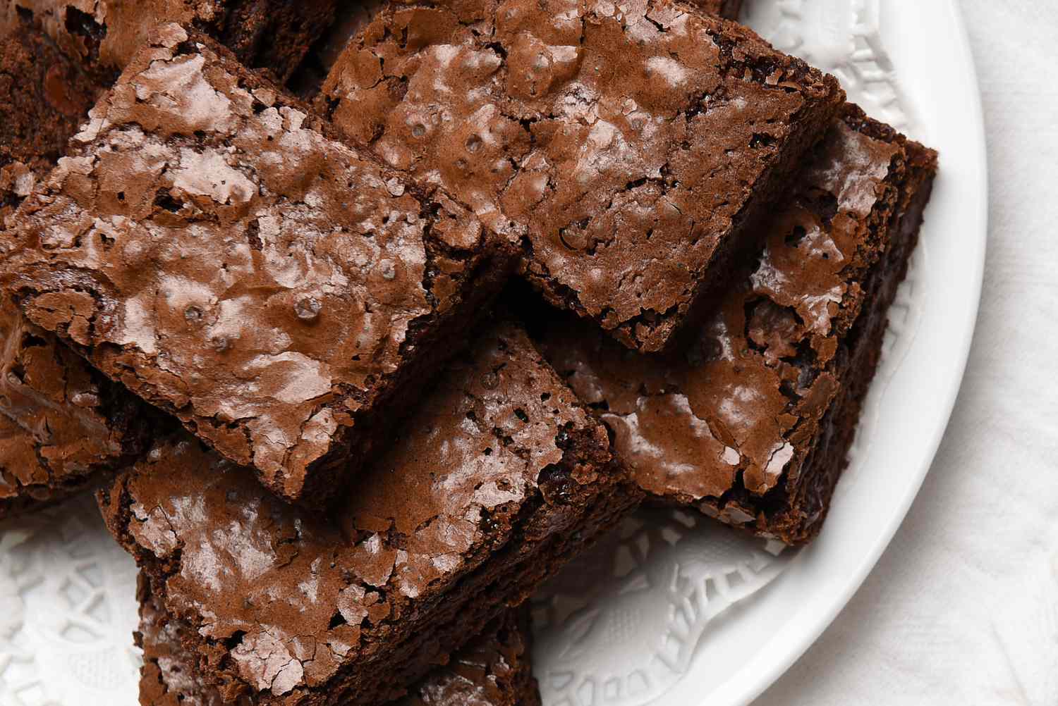 Flat lay view of a plate of fresh homemade brownies on a white plate, towel and wood kitchen table