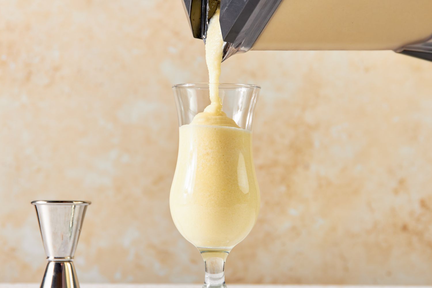 PiÃ±a Colada Poured Into a Hurricane Glass From the Blender and Next to It, a Jigger