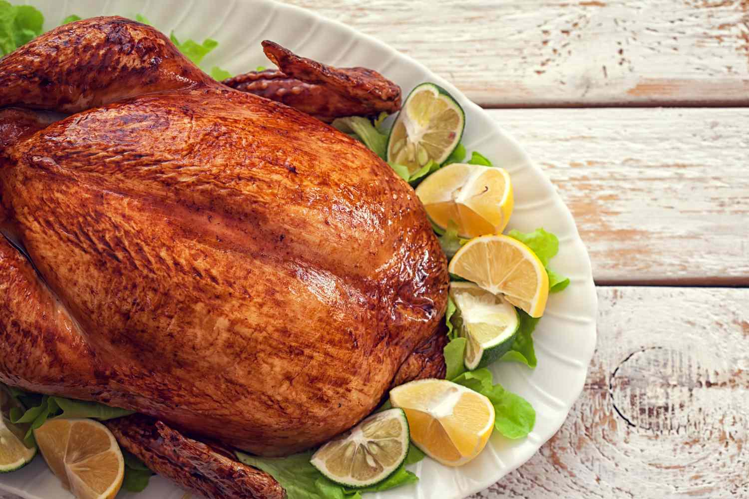 A roasted turkey on a white serving platter, garnished with lemon wedges and lettuce leaves