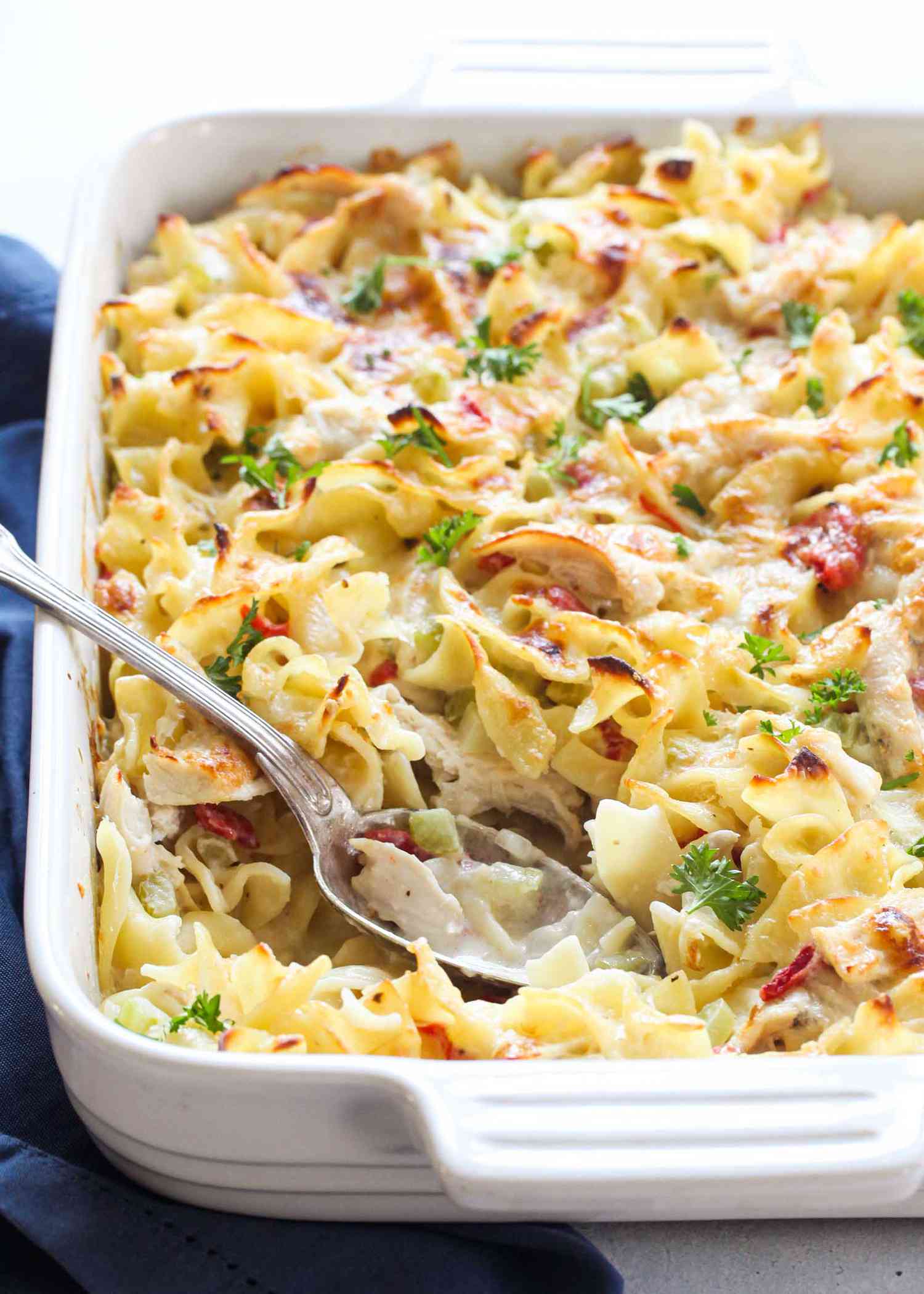Creamy Chicken Noodle Casserole in a white baking dish with a silver spoon.
