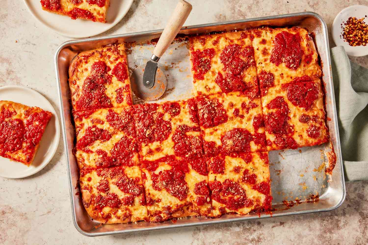 Grandma pizza slices in a sheet pan with some slices on plates surrounding the sheet pan