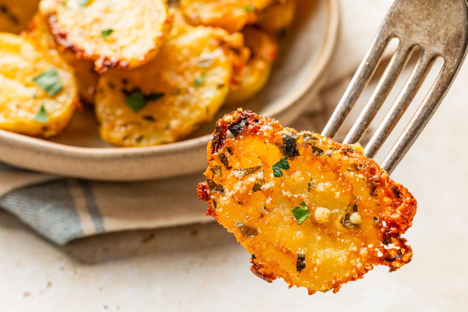 crispy parmesan potato on a fork, and in the background, the rest of the potatoes on a platter