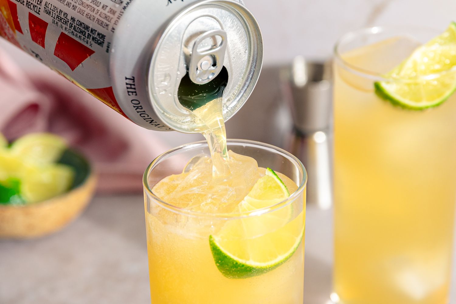 Beer can being poured into orange cocktail (Mezcal Shandy) on ice in a glass garnished with lime