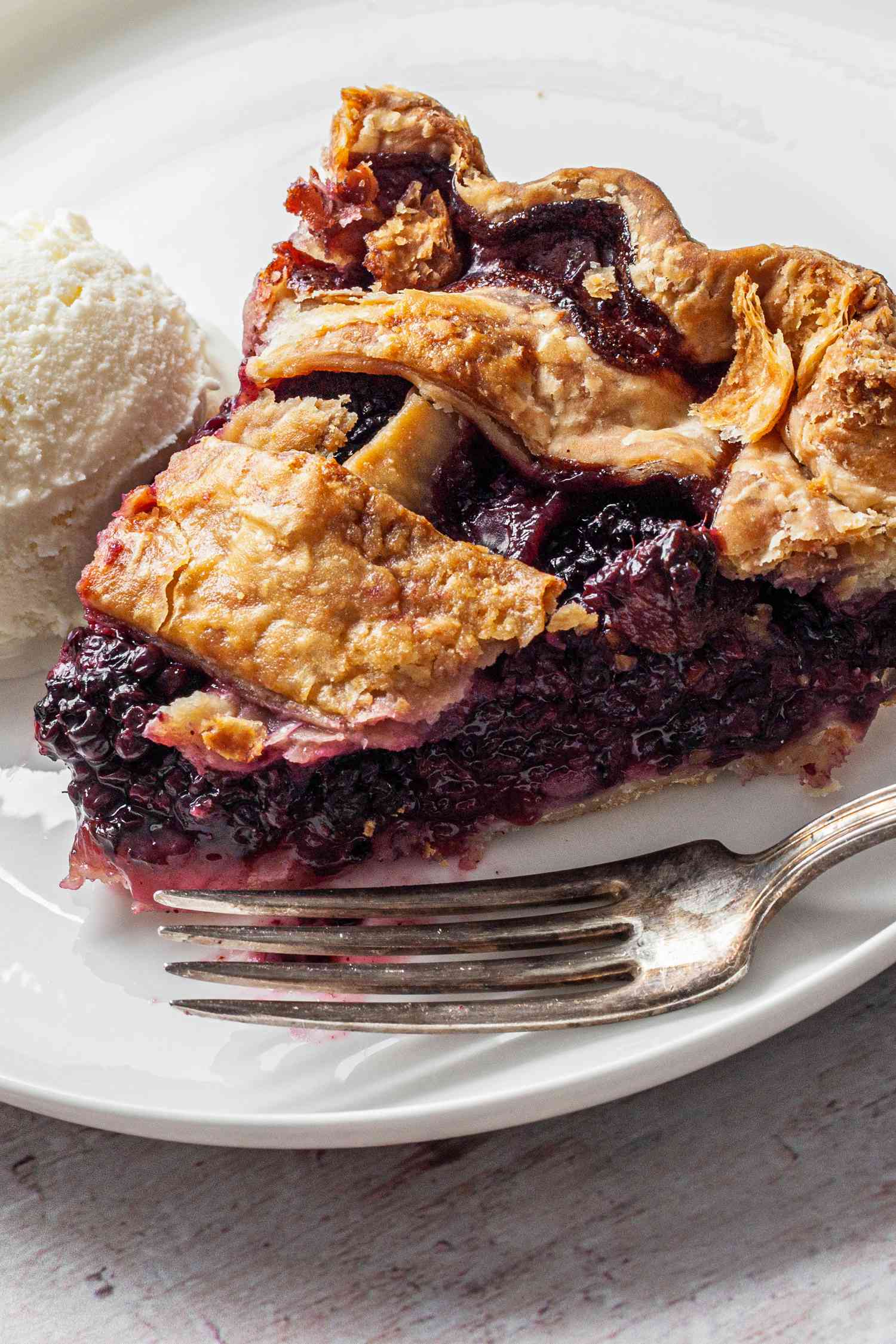 Slice of Blackberry Pie Served with a Dollop of Ice Cream on a Small Plate with Utensils