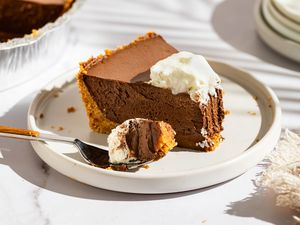 A slice of chocolate cream pie on a plate topped with whipped cream with a forkful taken out