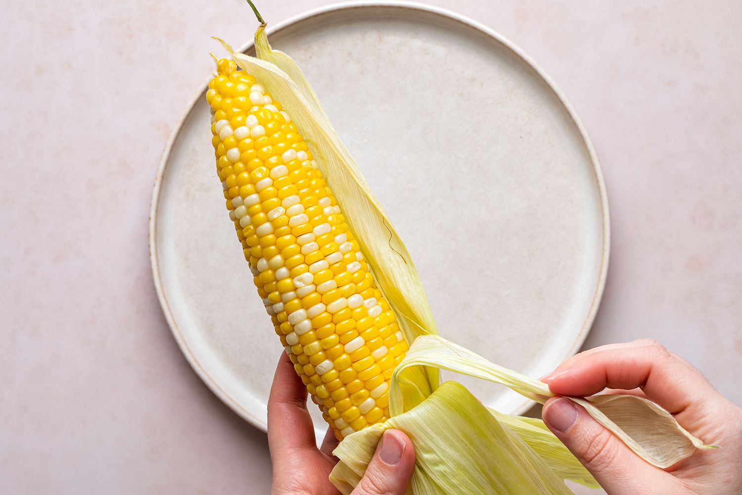 hands peeling husk off of microwaved corn cob