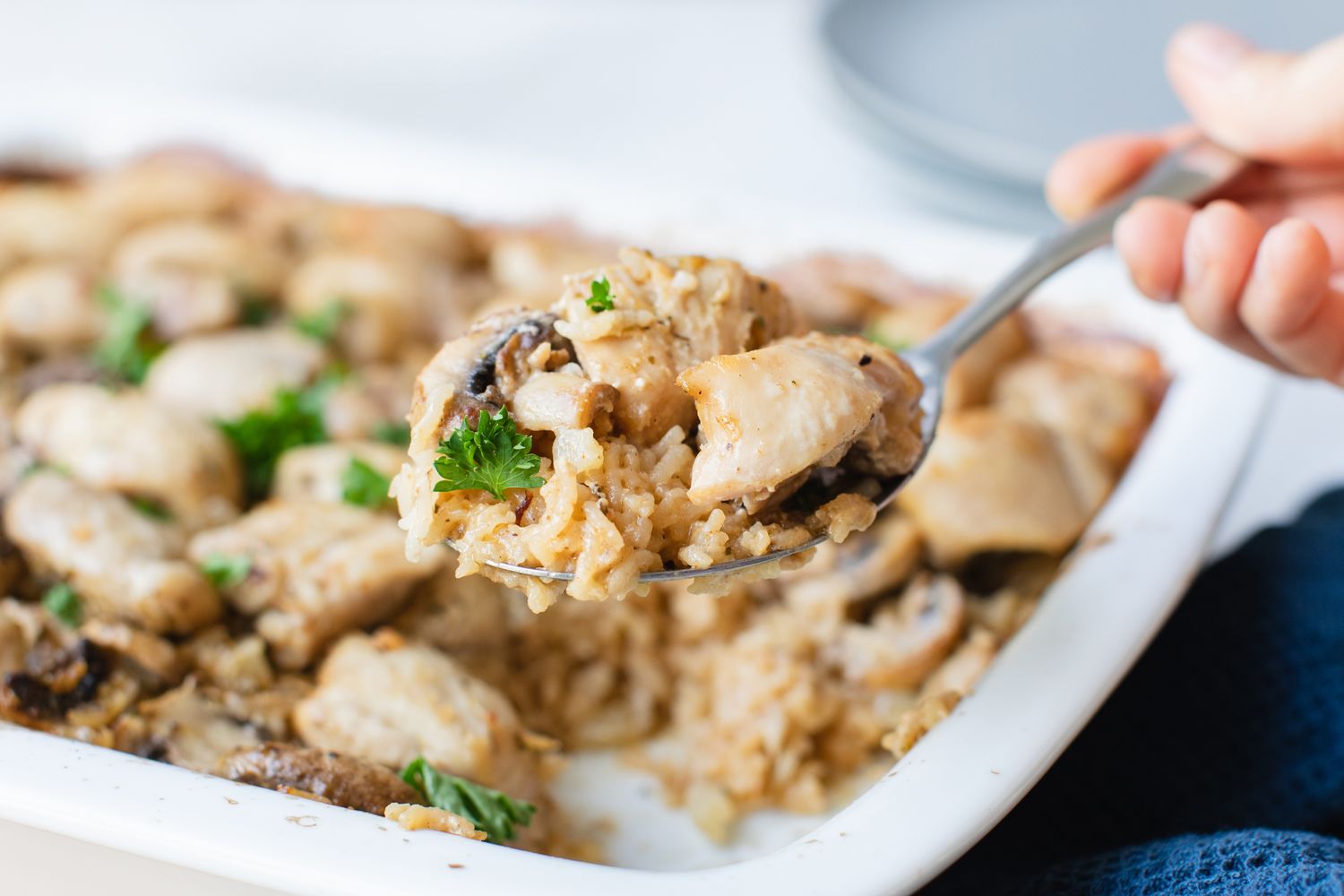 A spoon scooping casserole from a dish with mushrooms and garnish visible in the serving